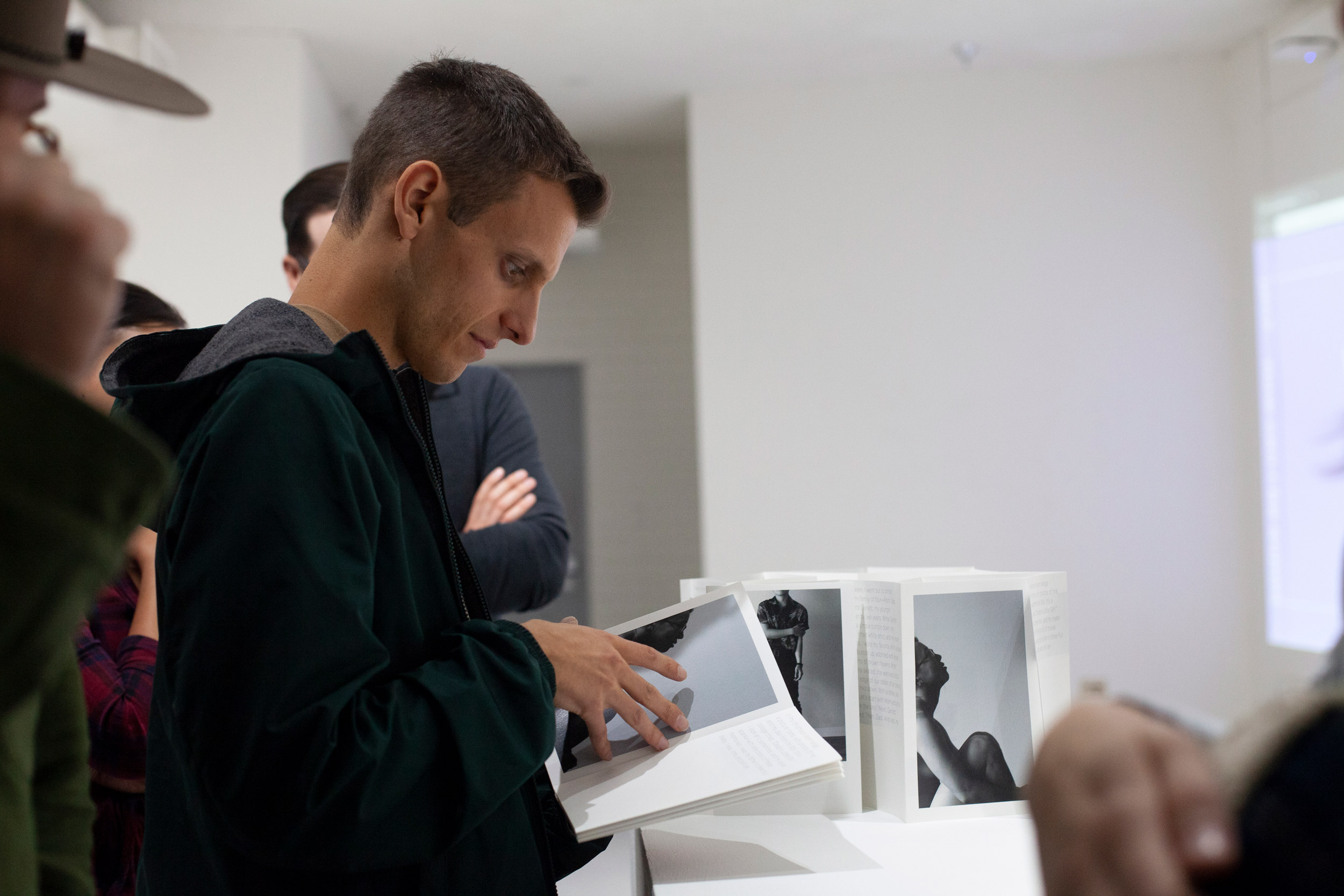 people in an exhibition space, one individual holding a folding book of black and white photographs